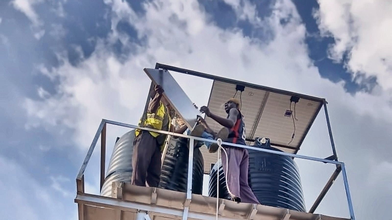 Two technicians fitting the solar array above the water tanks